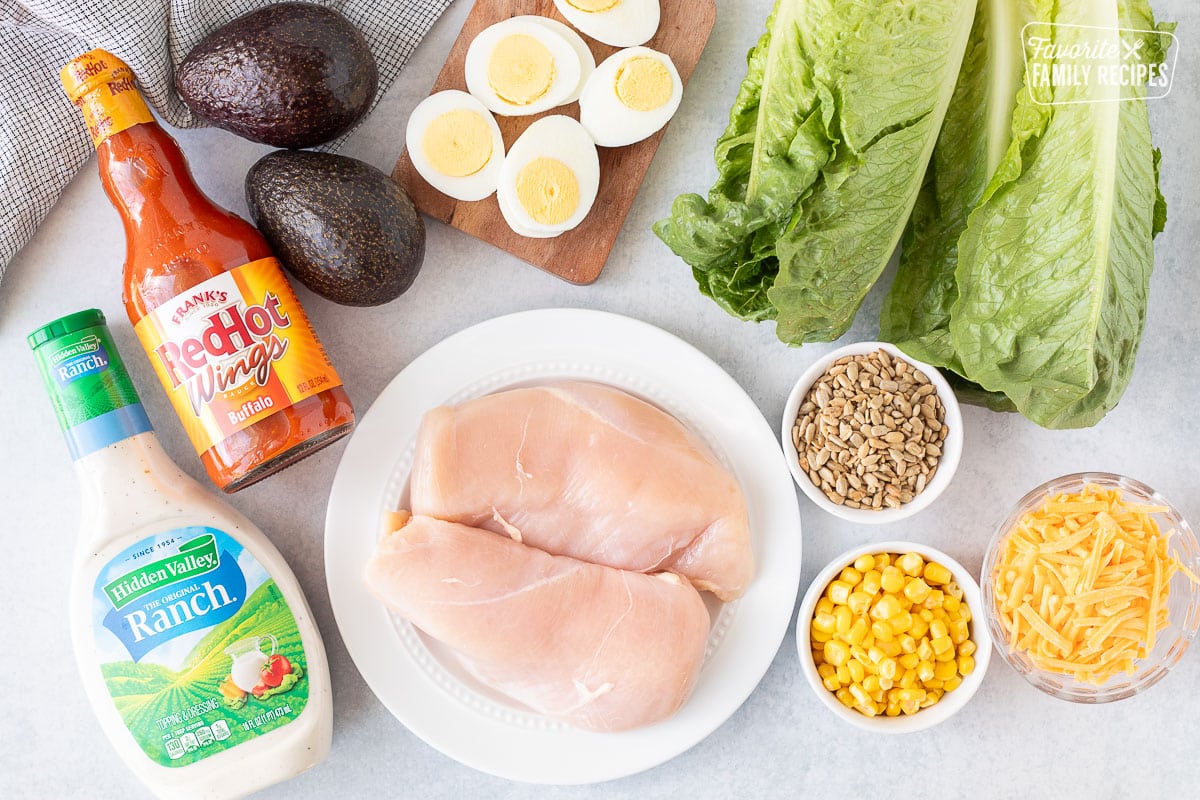 Ingredients to make Buffalo Chicken Salad including chicken, eggs, corn, cheese, sunflower seeds, lettuce, avocado, Frank's Red Hot Wings Buffalo and Ranch dressing.