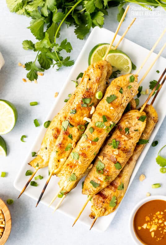 Plate with Chicken Satay garnished with cilantro, green onions and peanuts. Sliced limes on the side.