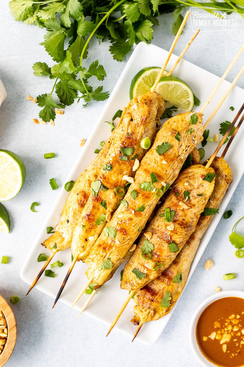 Plate with Chicken Satay garnished with cilantro, green onions and peanuts. Sliced limes on the side.