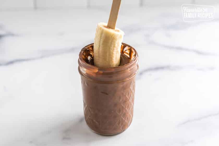 a frozen banana being dipped in chocolate