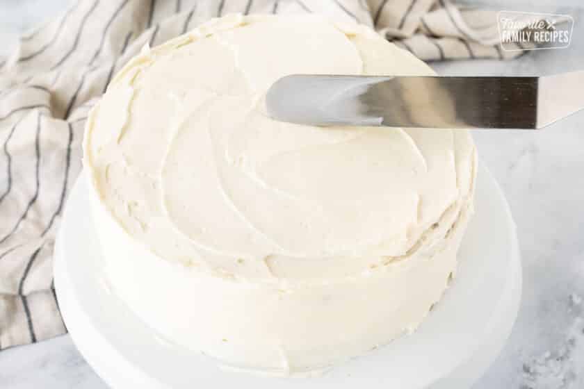 Spreading frosting with a spatula on top of a Hummingbird Cake.