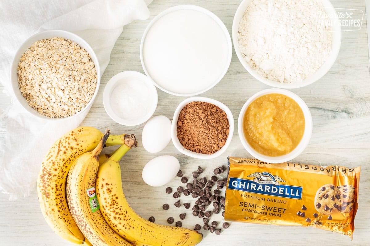 Ingredients to make Healthy Chocolate Chip Muffins including flour, sugar, cocoa powder, applesauce, chocolate chips, eggs, bananas, baking powder, baking soda, salt and oatmeal.