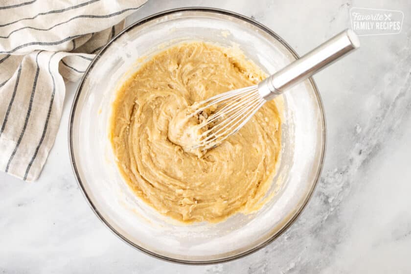 Glass mixing bowl with wet ingredients combined with a whisk.