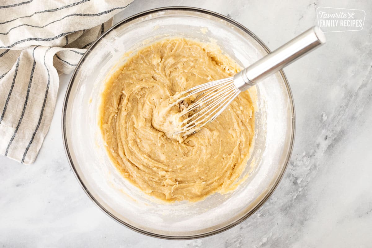 Glass mixing bowl with wet ingredients combined with a whisk.