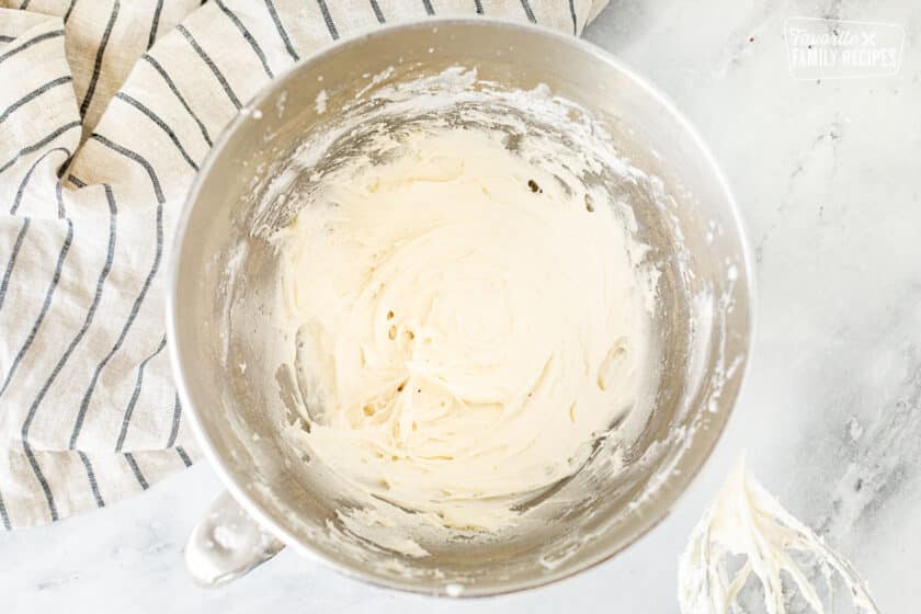 Cream cheese frosting in a mixing bowl with a mixing whisk on the side.