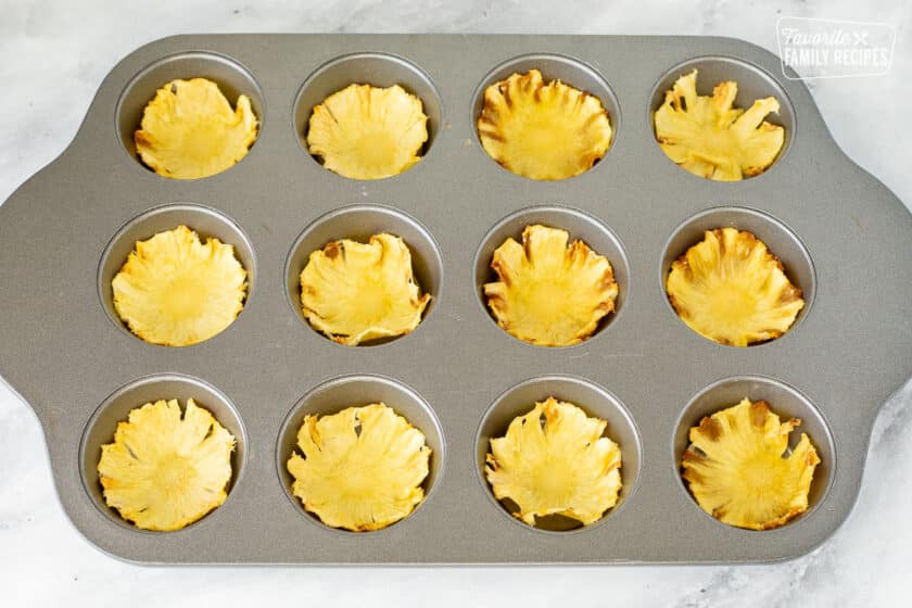 Dried pineapple slices cooling in a cupcake pan.