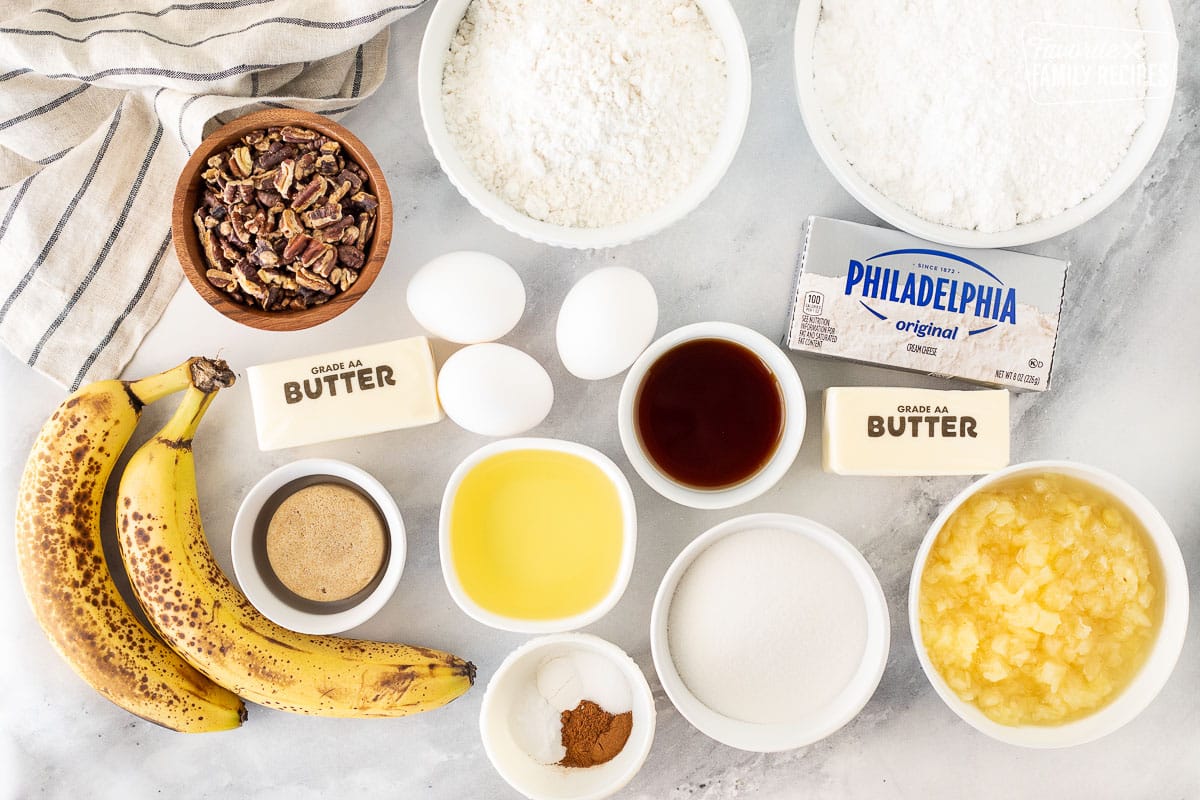 Ingredients to make Hummingbird Cake including flour, powdered sugar, brown sugar, butter, pineapple, cream cheese, cinnamon, baking powder, baking soda, oil, eggs, sugar, bananas and toasted pecans.