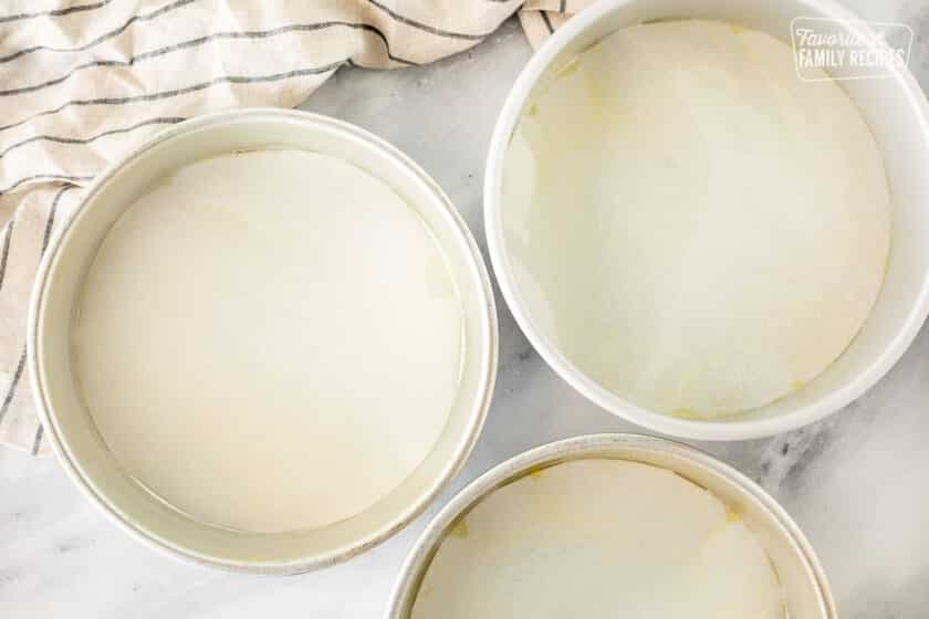 Three round cake pans lined on the bottom with parchment paper.