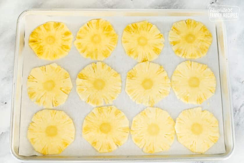 Thinly sliced pineapple on a baking sheet lined with parchment paper.