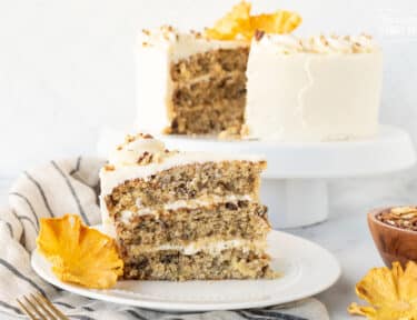 Slice of three layered Hummingbird Cake on a plate with a dried pineapple flower.