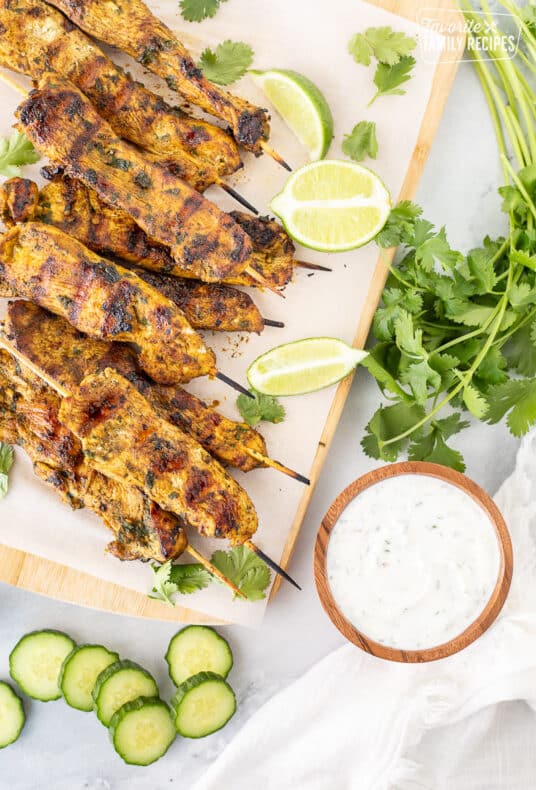 Grilled Thai chicken skewers on a wooden board with cucumber yogurt dip.