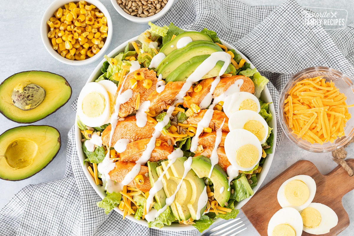 Bowl of Buffalo Chicken Salad with avocado, corn, seeds, cheese, eggs and dressing.