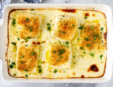 Baking dish with five pieces of Baked Cod in Cream Sauce garnished with parsley.