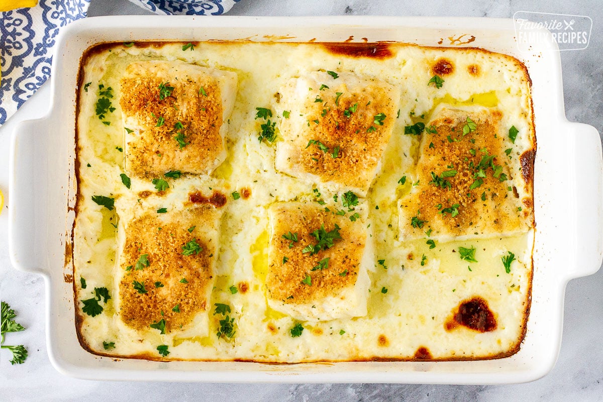 Baking dish with five pieces of Baked Cod in Cream Sauce garnished with parsley.