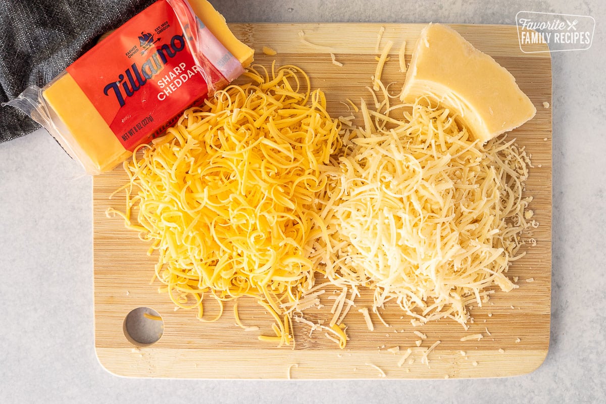 Cutting board with shredded sharp cheddar cheese and parmesan cheese.