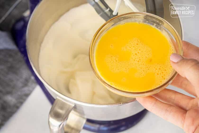 Hand holding whisked eggs in a small glass bowl of electric mixer bowl.