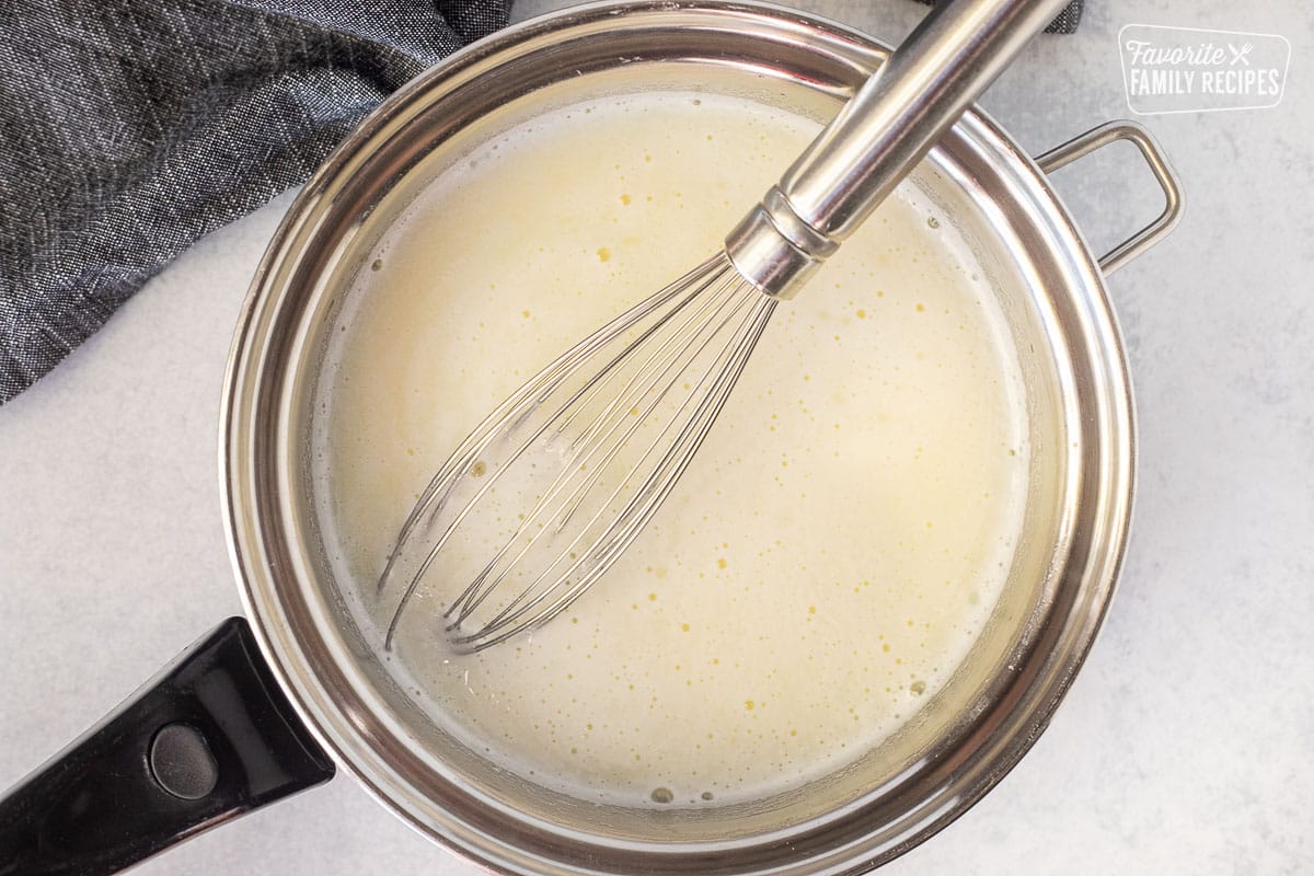Saucepan with whisk and milk mixture bubbling.
