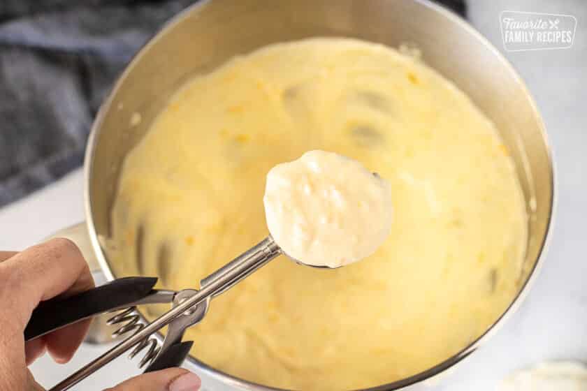 Cookie scoop holding Brazilian bread dough over a mixing bowl.