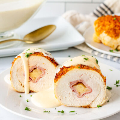 Chicken Cordon Bleu Sauce poured over Chicken Cordon Bleu cut in half on a plate.