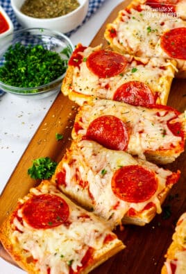 French bread pizza slices with herbs, pepperoni, and melted mozzarella, served on a wooden board with parsley and seasonings in bowls