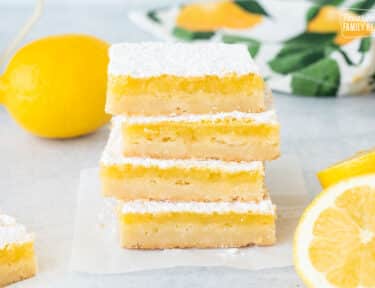 Stacked Lemon Bars next to fresh sliced lemons.