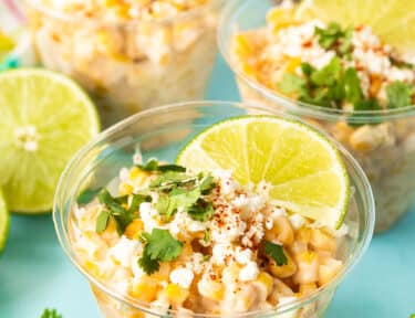 Three cups of Elote garnished with lime wedge, cilantro cojita cheese and chili powder.