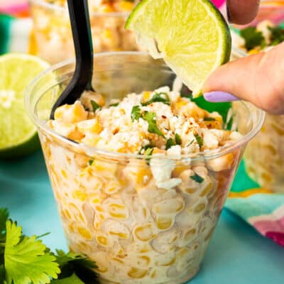 Hand squeezing a lime into Elote in a a cup.