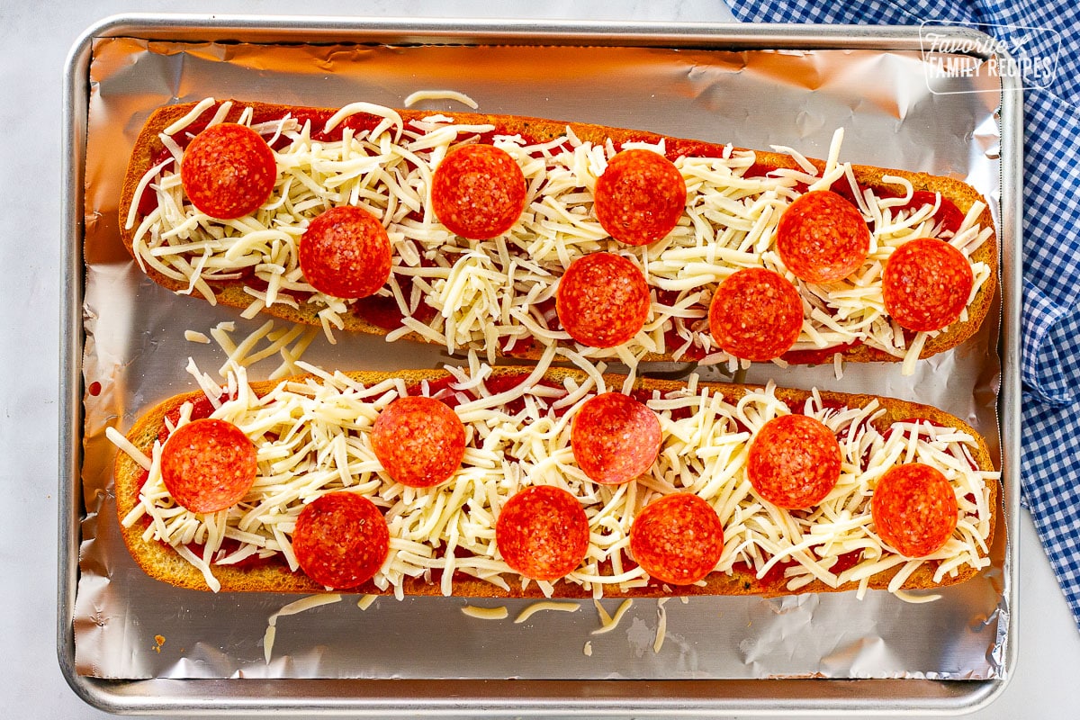 Two halves of French bread topped with sauce, cheese and pepperoni on a sheet pan.
