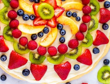 Easy dessert pizza topped with cream cheese icing and fresh fruit with extra fruit on the side.