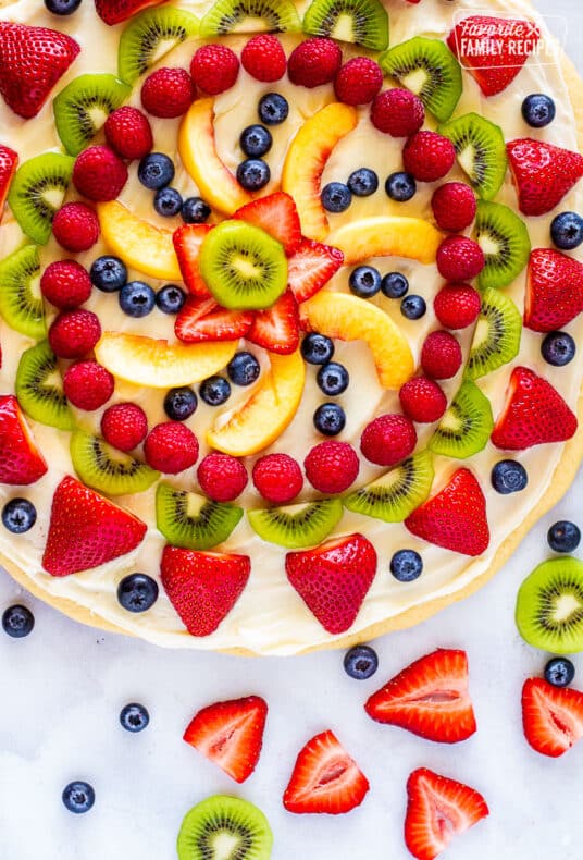 Easy dessert pizza topped with cream cheese icing and fresh fruit with extra fruit on the side.