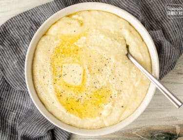 Spoon resting in a bowl of Grits with melted butter and pepper.