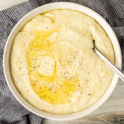 Spoon resting in a bowl of Grits with melted butter and pepper.