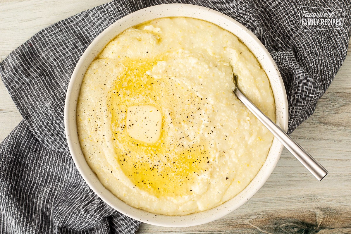 Spoon resting in a bowl of Grits with melted butter and pepper.