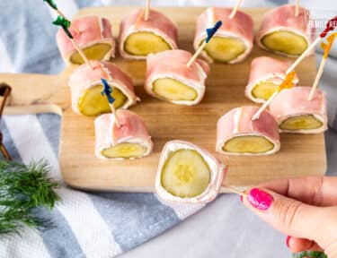 A ham and pickle roll up being picked up by a toothpick