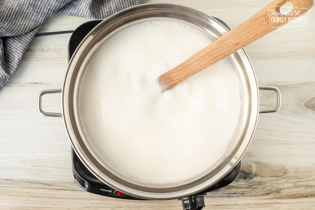 Saucepan with boiling milk mixture and wooden spoon.