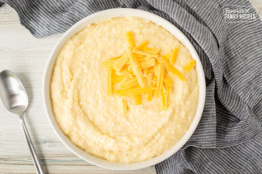 Bowl of Cheesy Grits with shredded cheese on top and spoon on the side.