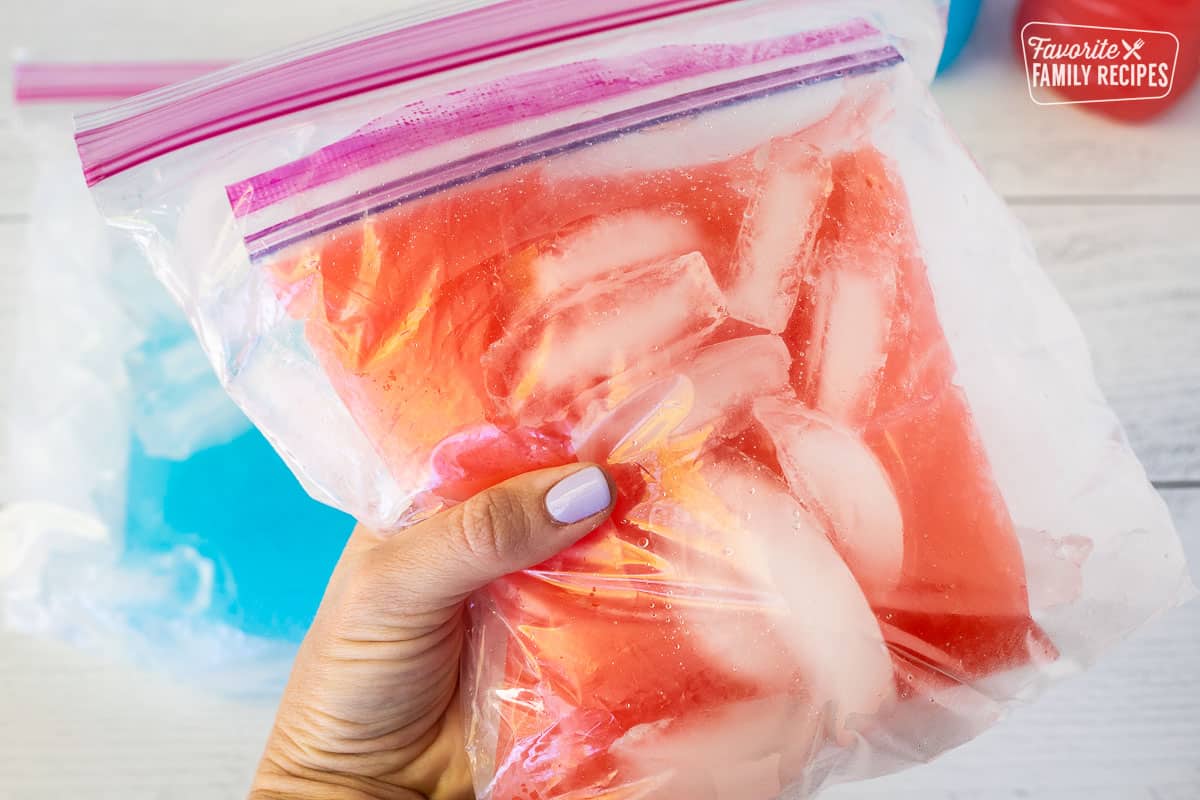 Hand holding and shaking a bag of juice inside a ziplock bag of ice and rock salt.