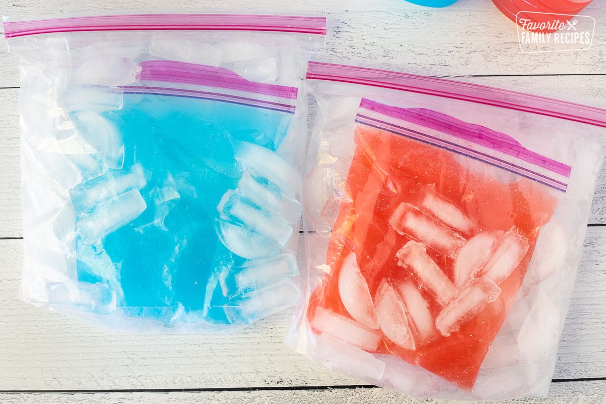 Blue juice and pink juice inside bags that are inside ziplock bags of ice and rock salt.