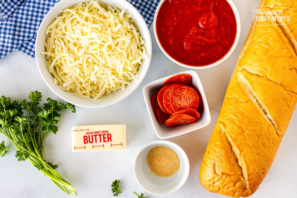 Ingredients to make French Bread Pizza including mozzarella cheese, tomato sauce, pepperoni, French bread, garlic powder, butter and parsley.