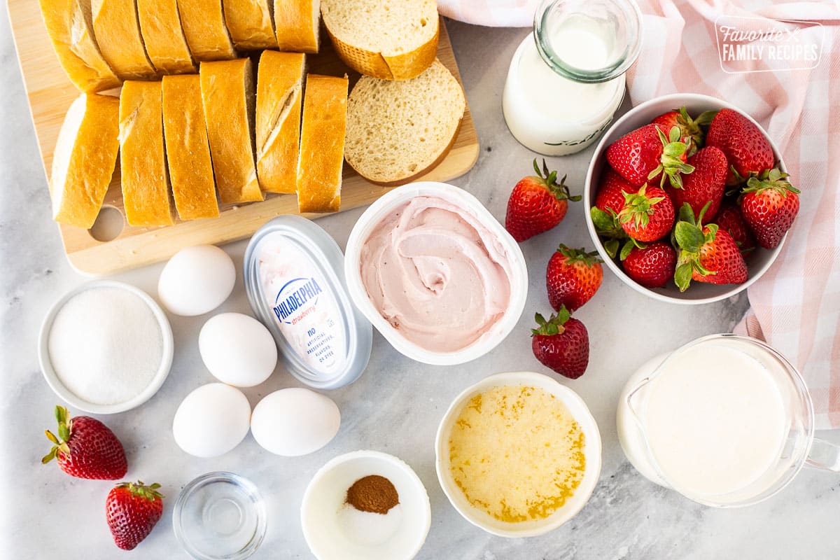 Ingredients to make Strawberry French Toast including French bread, strawberries, milk, cream, butter, cinnamon, salt, sugar, eggs, almond extract and strawberry cream cheese.