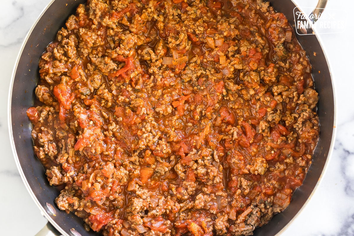 Brown beef, tomatoes, and onions in a skillet