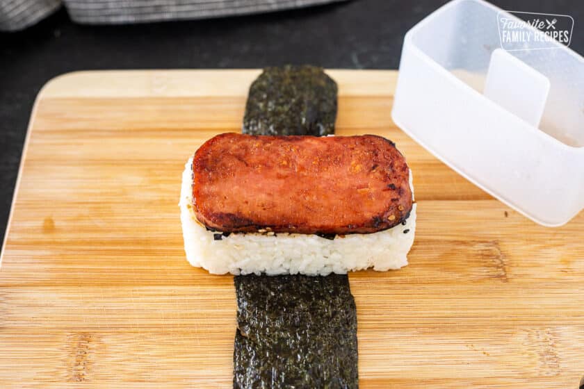 Musubi mold next to an unwrapped Spam Musubi showing how to mold the rice to the shape of the spam.