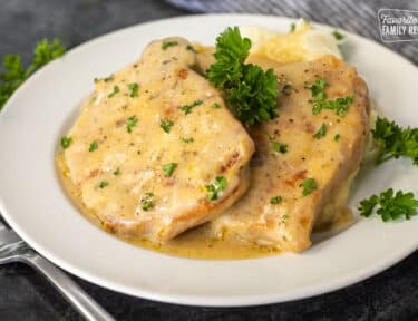 Dinner plate with melt-in-your-mouth pork chops with savory gravy garnished with parsley.