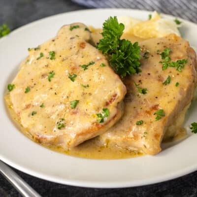 Dinner plate with melt-in-your-mouth pork chops with savory gravy garnished with parsley.