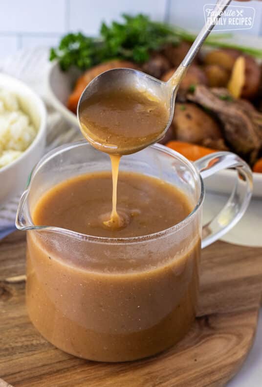 Pouring Beef Gravy into a glass container of gravy. Mashed potatoes and vegetables in the background.