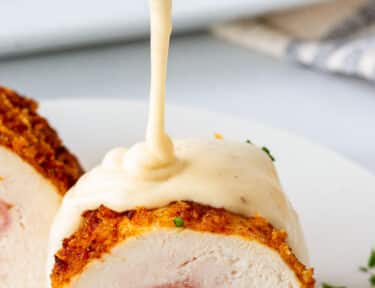 Pouring Chicken Cordon Bleu Sauce over a piece of Chicken Cordon Bleu.