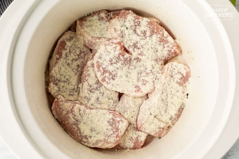 Raw pork chops in a slow cooker with ranch dressing sprinkled on top for crock pot pork chop recipe.