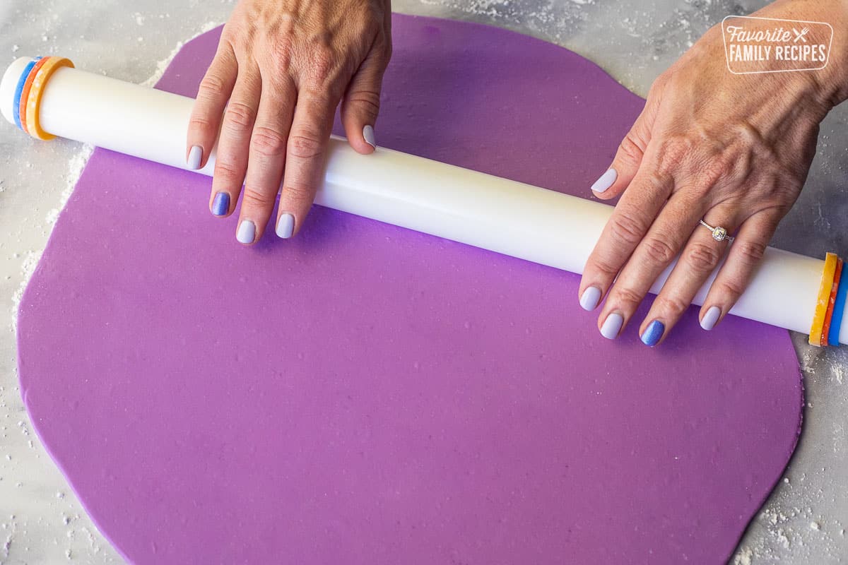 Rolling out a purple sheet of fondant with a roller.