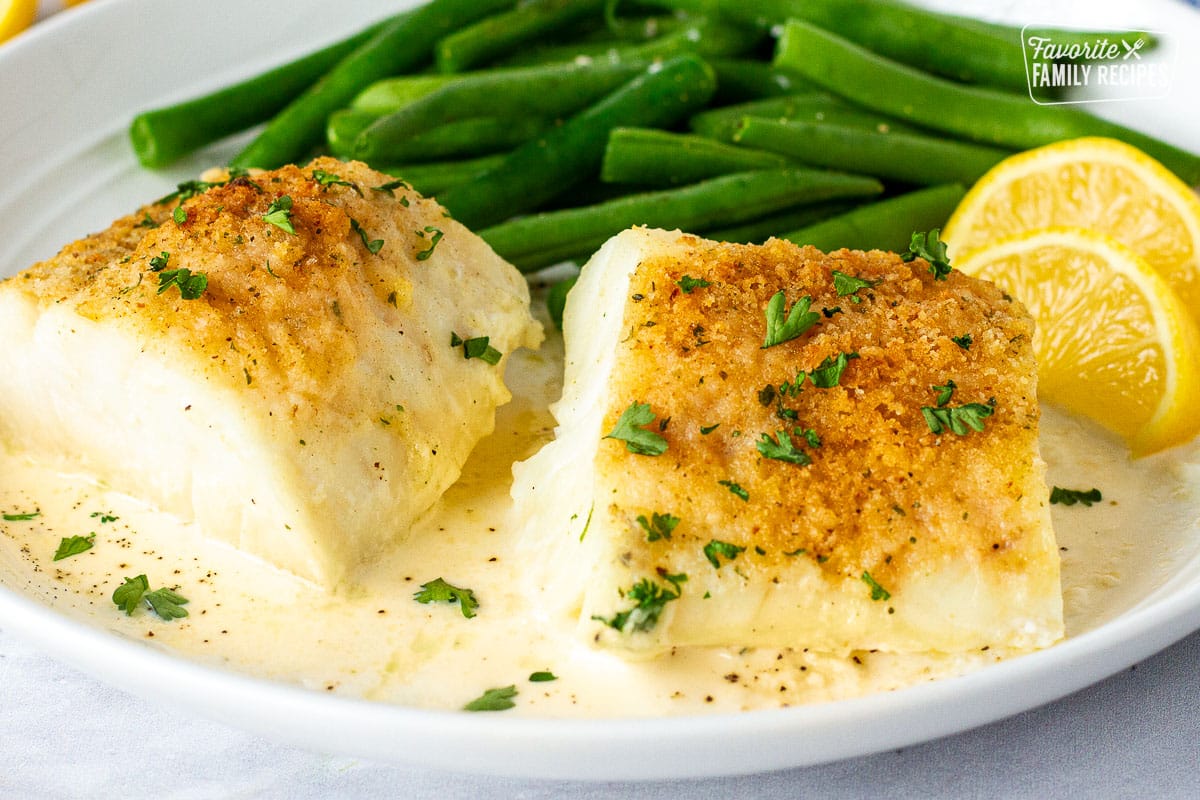 Plate of Baked Cod in Cream Sauce served with green beans and lemon wedges.