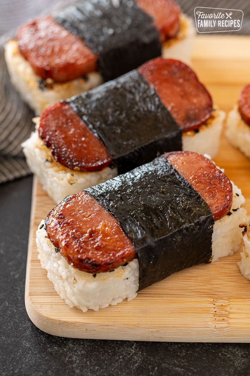 Three freshly made Spam Musubi lined up on a cutting board, ready to eat.